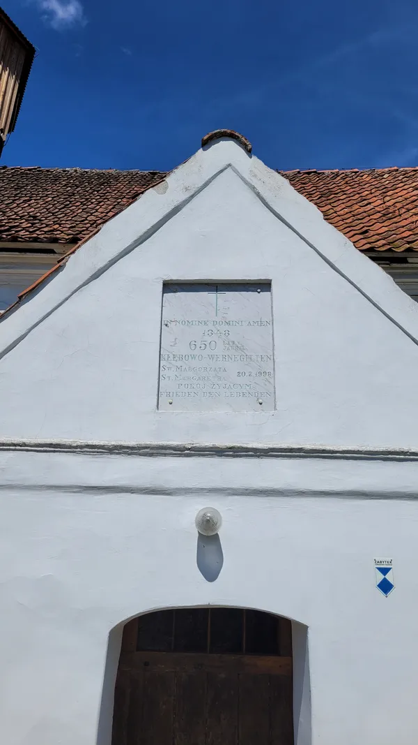 Tablica upamiętniająca 650-lecie wsi (1348-1998): „IN NOMINE DOMINI AMEN · 650 lat · Kłębowo-Wernegitten · św. Małgorzata · 20.7.1998 · Pokój żyjącym / Frieden den Lebenden”.